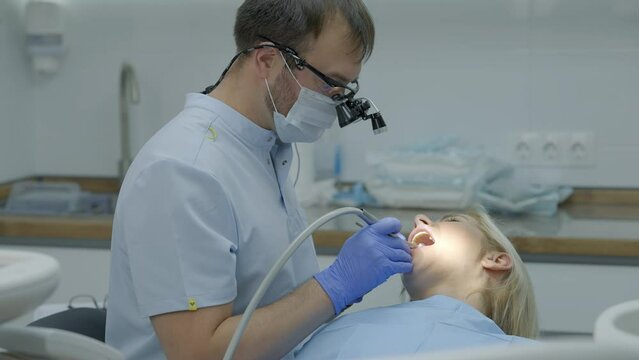 Male dentist drills tooth to female patient in dental chair. Slow motion