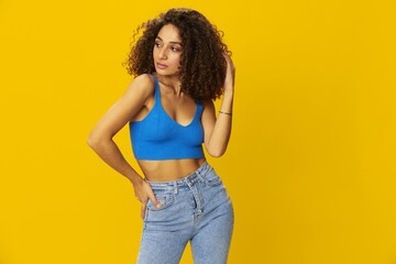 Woman with curly afro hair in a blue t-shirt on. yellow background signs with her hands, look into the camera, smile with teeth and happiness, copy space