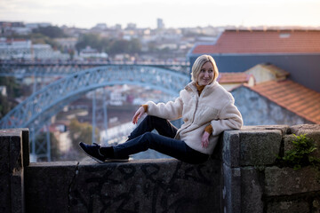Fototapeta na wymiar A female tourist sits on a masonry wall in Porto, Portugal..