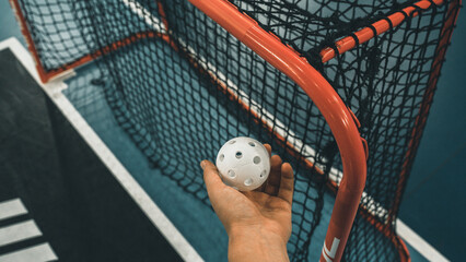 Hand holding a Floorball ball next to goal post
