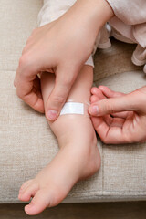 Mother woman sticks a medical adhesive plaster on the toddler baby leg. Mom s hand with sticky wound protection tape and child s foot. Kid aged one year and three months