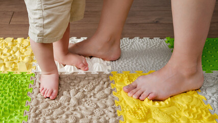Baby toddler foots and woman mother on a medical orthopedic mat. Child and adul parent legs with...