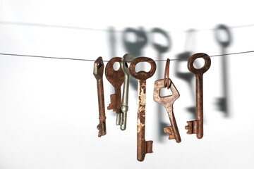 A different old retro rusty keys from different locks hanging on string with a drop shadow on a white wall