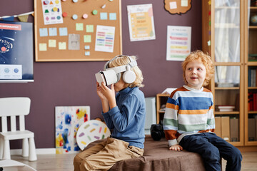Little boy in vr headset watching video and playing virtual game while sitting next to happy...