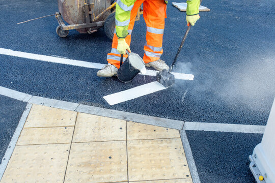 Road workers applying hot melt traffic resistant paint for white, yellow and red road marking lines on new build asphalt road