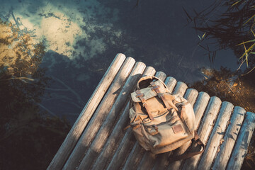 Backpack of traveller on wooden pier near summer tranquil lake. View from above.