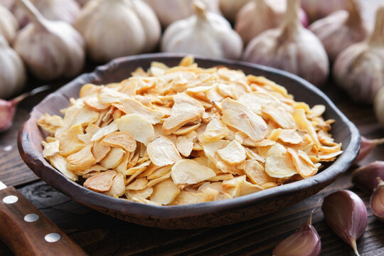 Bowl of dried garlic flakes, garlic cloves. Heads of garlic on background. Dried seasoning.