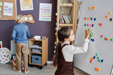 Clever learner of primary school cleaning whiteboard with plastic letters of English alphabet while compilating new words in classroom