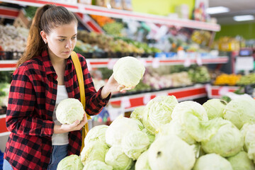 Portrait of a young female customer in a store near the counter, choosing cabbage to buy