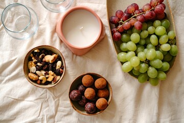 Top view of a mini dessert on a white tablecloth, chocolate truffles, grapes, legumes, and a candle