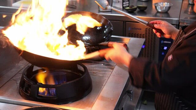 Chef in a restaurant kitchen stir fry meat in a wok lighting a large flame
