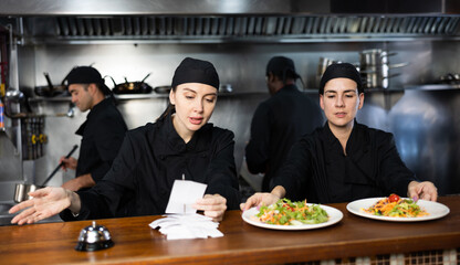 Portrait of two women chefs working in modern open kitchen, checking orders and giving out ready...