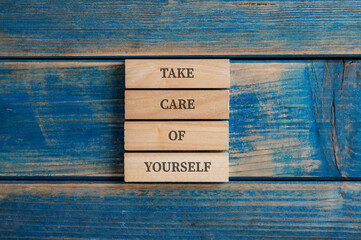 Take Care of Yourself sign written on four stacked wooden pegs