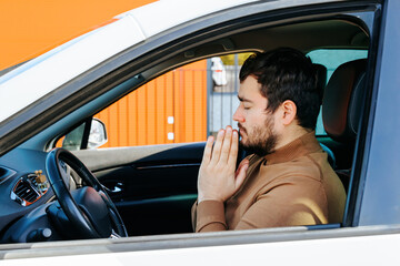A young man sits in a car with his eyes closed, hands folded and praying. On the face of a person...