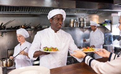 African american chef serving ready meals to visitors of restaurant