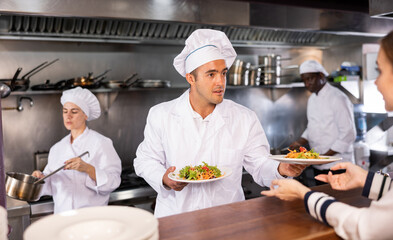 Service process in cafe - chef serves ready meals to visitors of restaurant