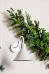 A decor made of Christmas tree branches hangs on the wall near a white sconce. Festive New Year's decor on the wall at home