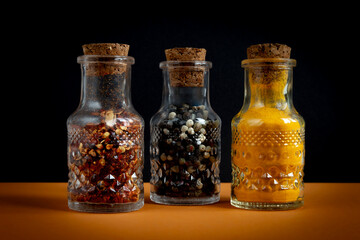 Spices in glass jars. Hot pepper, black pepper and curcuma powder in containers closed with corks.