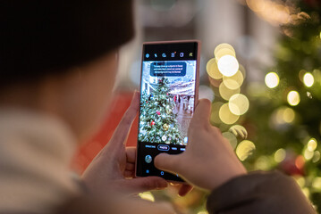 Girl photographs a Christmas tree, garlands and decorations on a smartphone