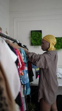 Black woman in a yellow durag  and an oversized dress shirt looking for an outfit in her wardrobe