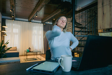 Obraz premium Tired female freelance has neck pain and a headache while working from home with tablet and laptop.