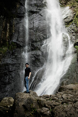male traveler with a beard on a hike against the backdrop of a waterfall in the mountains