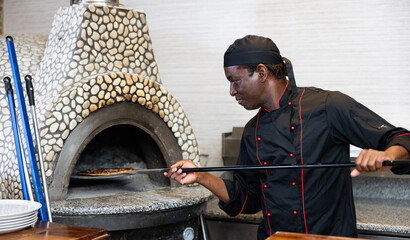 Portrait of cheerful pizza chef at work, man taking pizza from oven at restaurant kitchen
