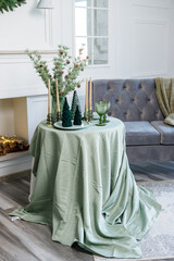 Table setting for Christmas or New Year's dinner with candles, decorations, tablecloth and napkins on the background of a Christmas tree in an apartment
