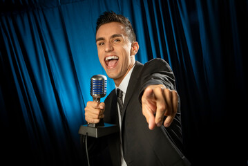 Man in business suit singing or yelling into a microphone  and pointing at the camera against a...