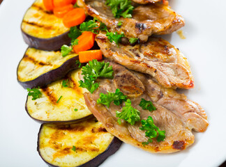 Delicious broiled lamb loin chops served on white plate with grilled eggplant and carrots..