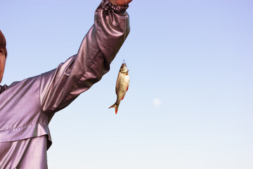 Fisherwoman holding in hand and showing a river fish caught on hook against blue sky. Sports,...