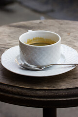 White coffee cup stands on saucer on round wooden table on cafe or restaurant terrace on a city street. Hot fragrant morning coffee and milk based drink. Espresso, cappuccino, latte, cortado in a cup.