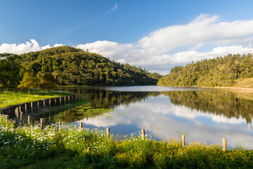 Obraz premium a beautiful view of a mountain with trees and a sky with clouds reflected in a lake
