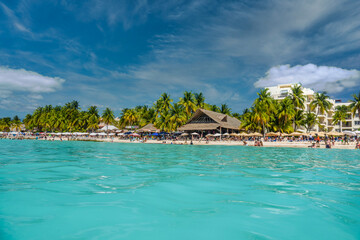 People swimming near white sand beach with umbrellas, bungalow bar and cocos palms, turquoise caribbean sea, Isla Mujeres island, Caribbean Sea, Cancun, Yucatan, Mexico