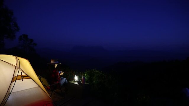 Asian woman camping on top of a mountain and taking pictures in the evening in the quiet darkness.