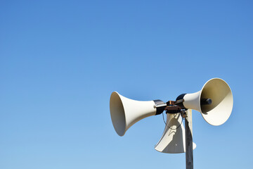 Old weathered vintage public address (PA) megaphone system loudspeaker and blue sky.