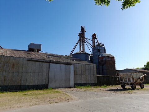 Silos con tolva para secadora y elevadora granos de con un cobertizo de metal de zinc acanalado oxidado junto a maquinaria de transporte, forma un original dise&ntilde;o industrial con fondo del cielo azul