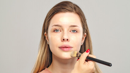 Makeup artist or stylist applies foundation or concealer to the face of the female model. Visagiste...