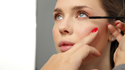 Make-up artist in photo studio doing makeup for beautiful girl. Woman making up using comb for...
