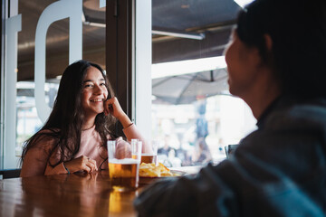 Two happy girls gossiping with each other in a bar. They are having some beers and snack