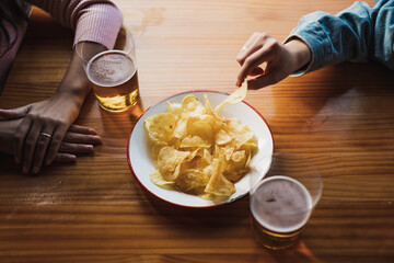 High angle shot of young woman taking a potato chip from plate. She is with a friend in a bar.
