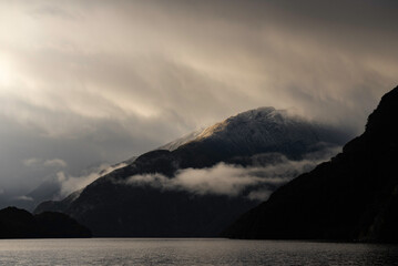 Dramatic and moody morning light illuminates a snow covered slope in the Doubtful Sound.