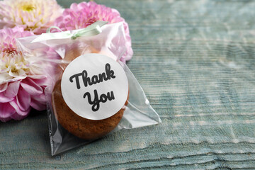 Bag of cookies with phrase Thank you and flowers on grey wooden table, space for text