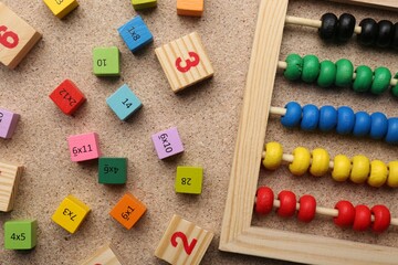 Wooden cubes with numbers and multiplications near abacus on fiberboard, flat lay