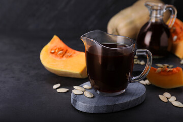 Fresh pumpkin seed oil in glass pitcher on dark grey table. Space for text