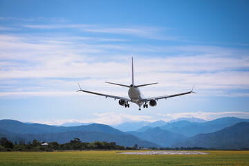 Fototapeta na wymiar Modern white airplane landing on runway near mountains