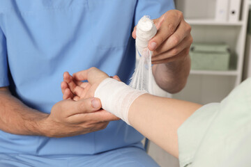 Obraz na płótnie Canvas Doctor applying bandage onto patient's wrist in hospital, closeup