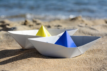 Two paper boats near sea on sunny day, closeup