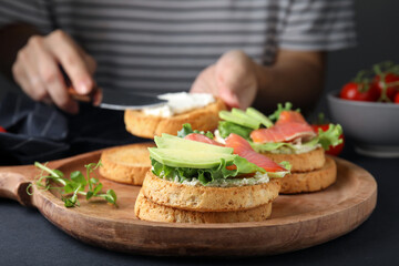 Woman making tasty rusks with salmon, cream cheese and avocado at black table, closeup