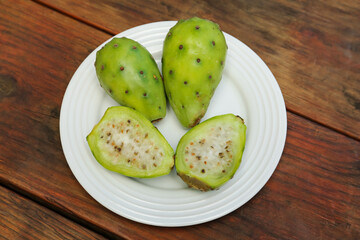 Tasty prickly pear cut and whole fruits on wooden table, top view
